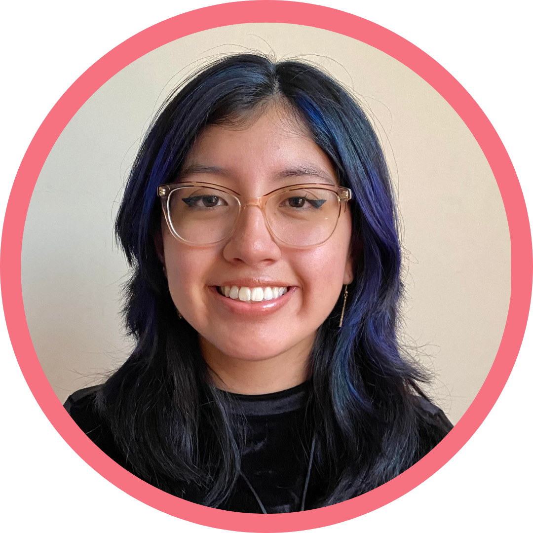 A woman in her 20s with blue hair and brown eyes, wearing a transparent-framed glasses and a black shirt.