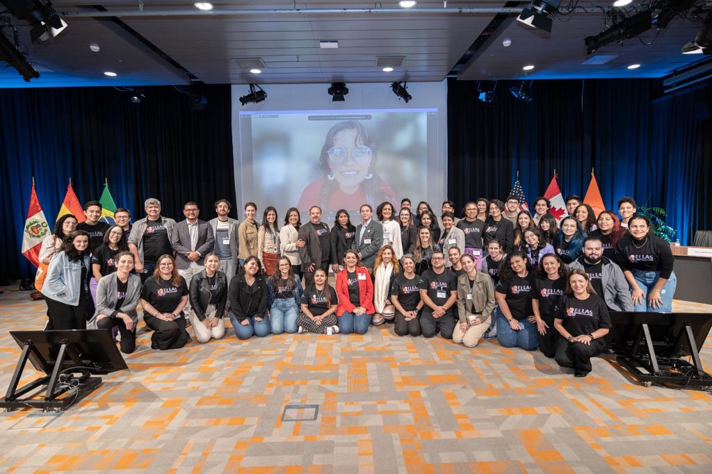 todos os membros do projeto que participaram do evento estão posando para foto. Ao centro da imagem é possível ver um banner do projeto.