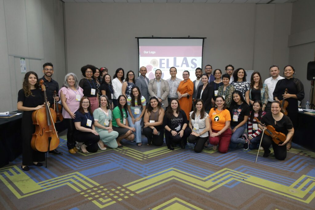 Membros do projeto posando para foto. Ao fundo é possível ver painel do ELLAS.