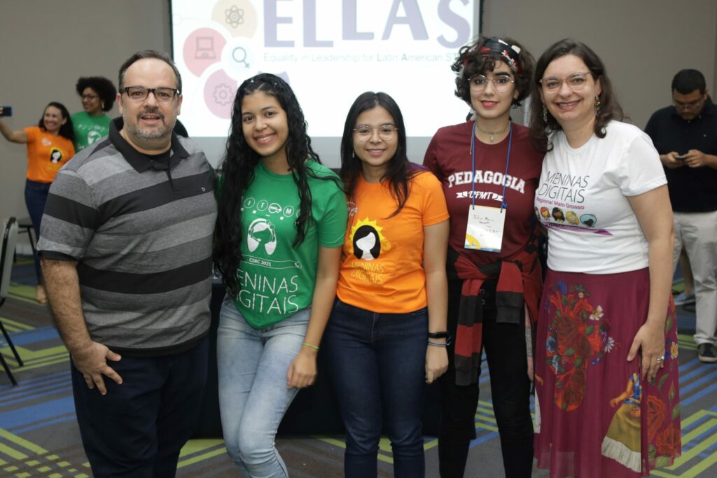 Membros do projeto posando para foto com o painel do ELLAS atrás.