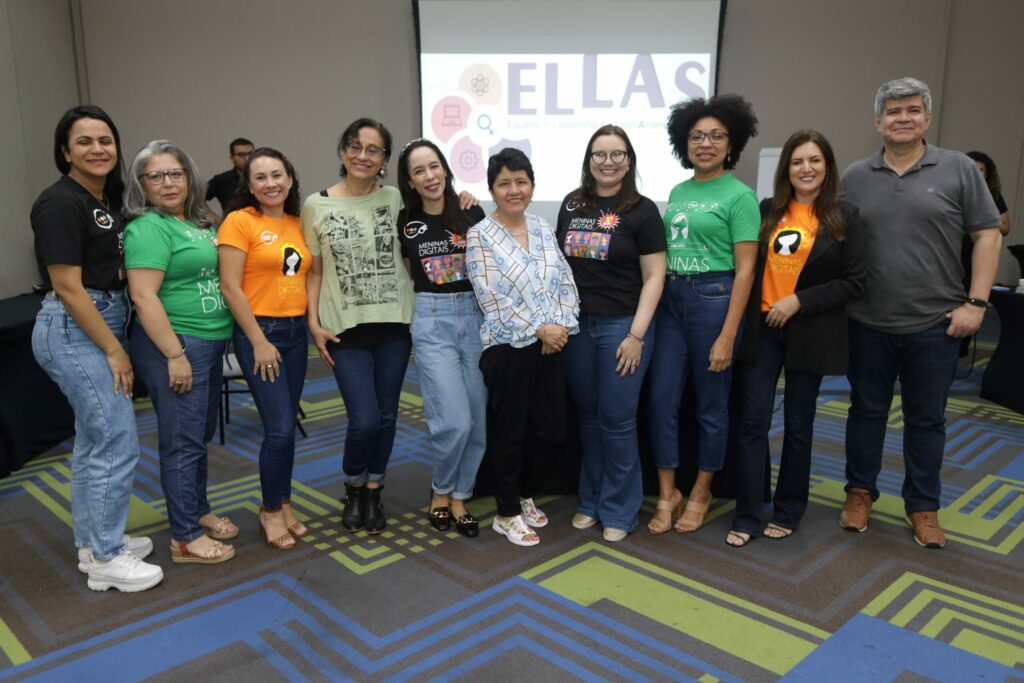 Membros do projeto posando para foto. Ao fundo é possível ver painel do ELLAS.