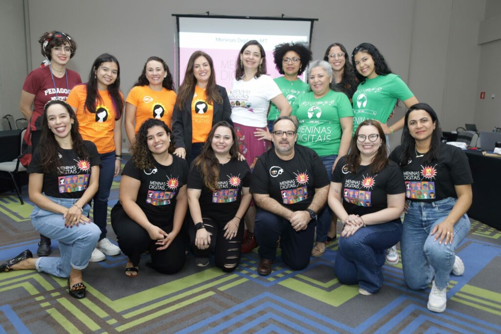 Membros do projeto posando para foto. Ao fundo é possível ver painel do ELLAS.